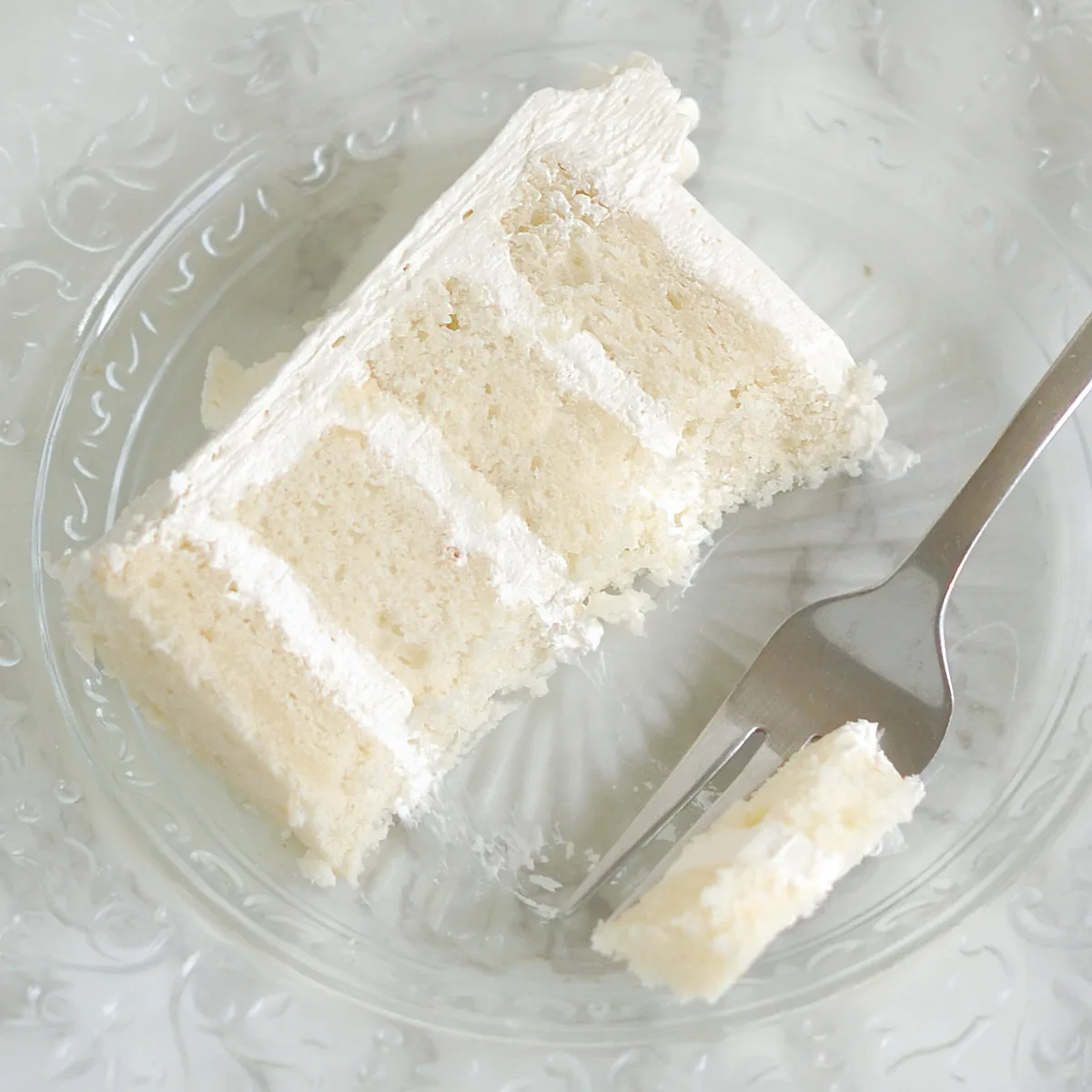 a slice of white cake on a glass plate with a fork.
