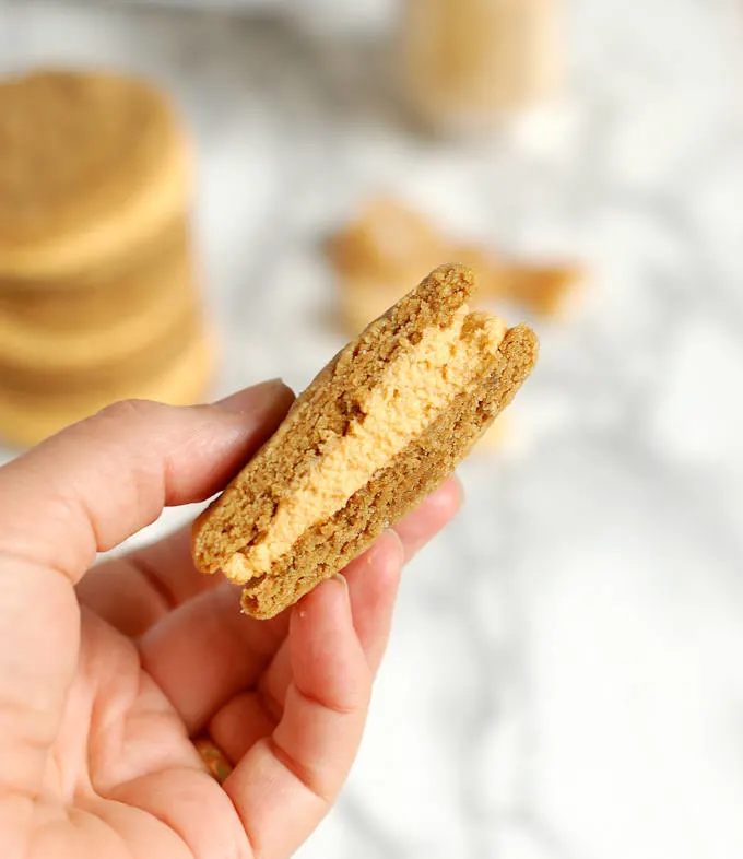 a hand holding a ginger sandwich cookie with pumpkin ganache filling