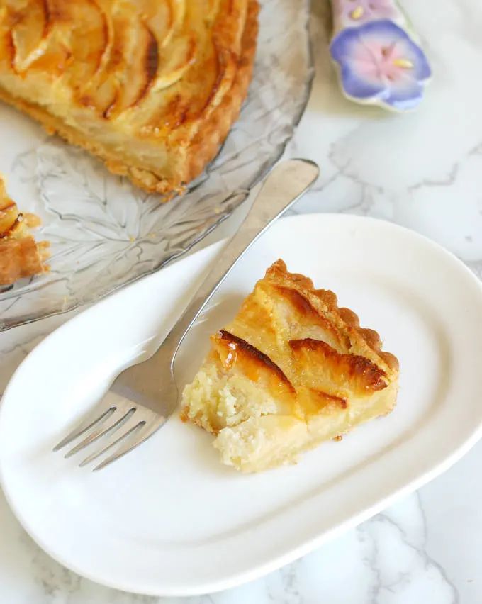a half eaten slice of Apple Frangipane Tart on an oval plate with a fork