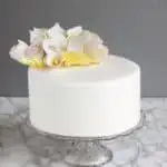 a fondant covered cake on a glass cake stand with sugar flowers