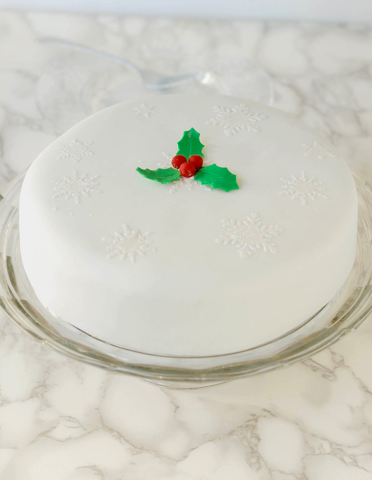 a fondant covered fruitcake with holly decorations on a cake plate.