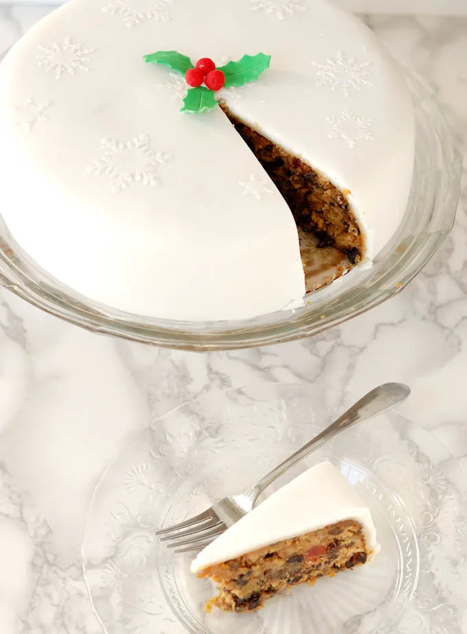 a sliced Brandy Aged Fruitcake on a glass cake stand with a slice of cake in the foreground