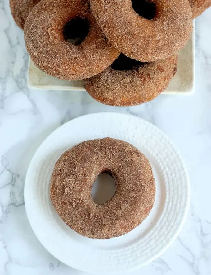 a sourdough donut on a white plate and a plate full of more donuts