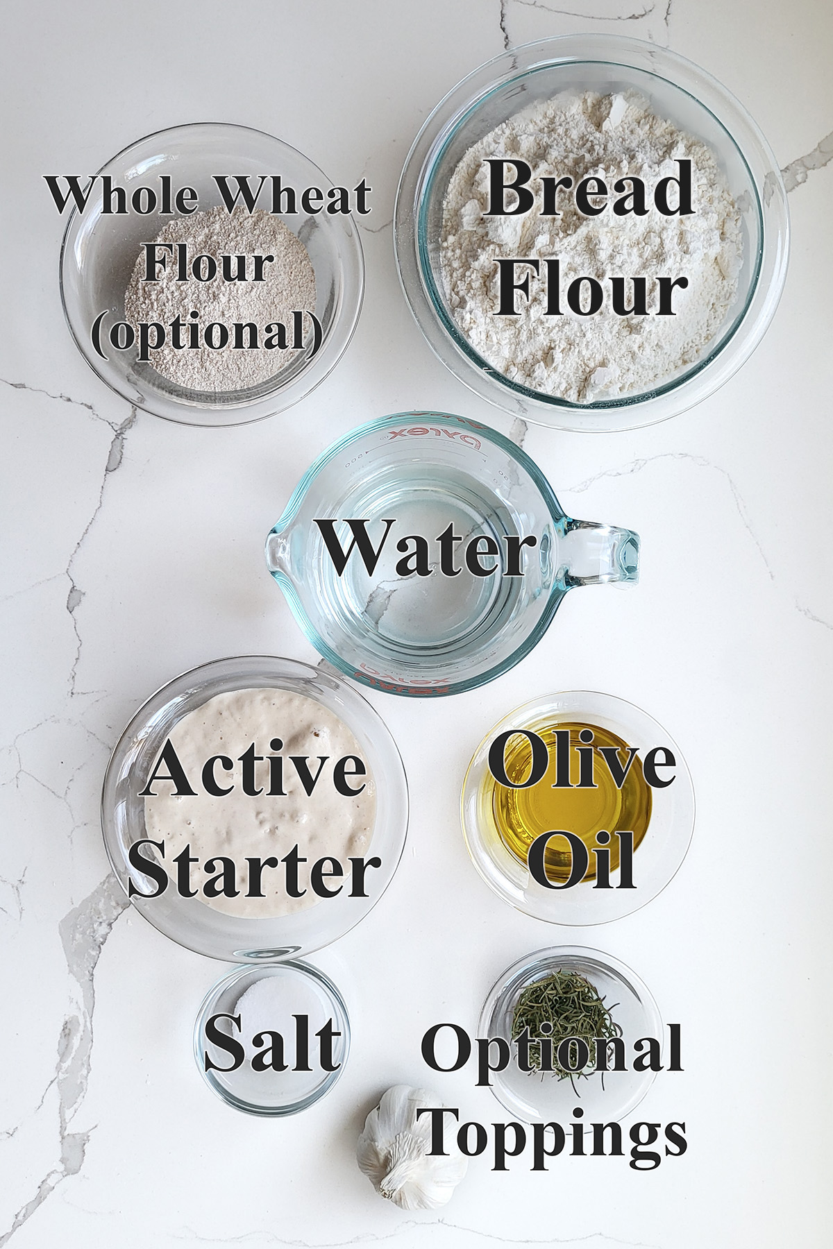 ingredients for sourdough focaccia in glass bowls on a white surface.