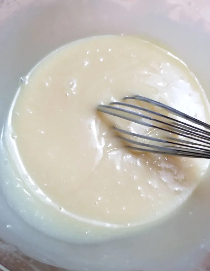 a whisk in a bowl of liquid white chocolate ganache