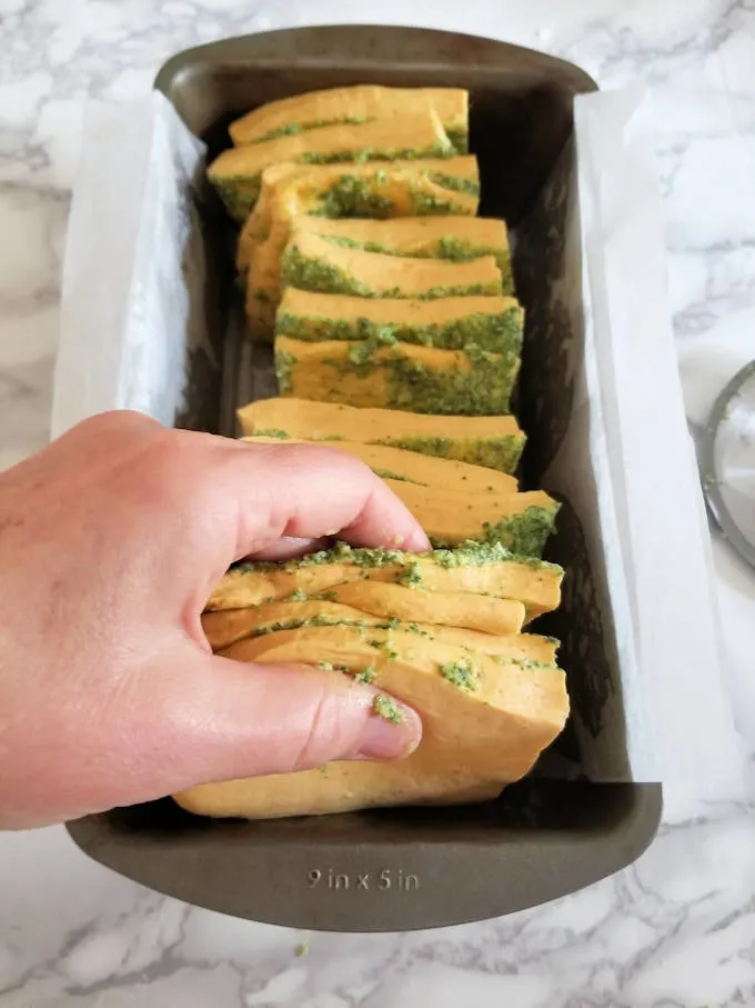 a hand stacking squares of pumpkin bread into a loaf pan
