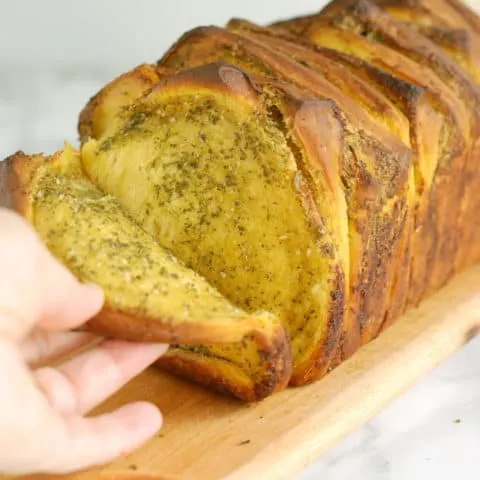 a hand pulling a slice of bread from pumpkin pull apart loaf