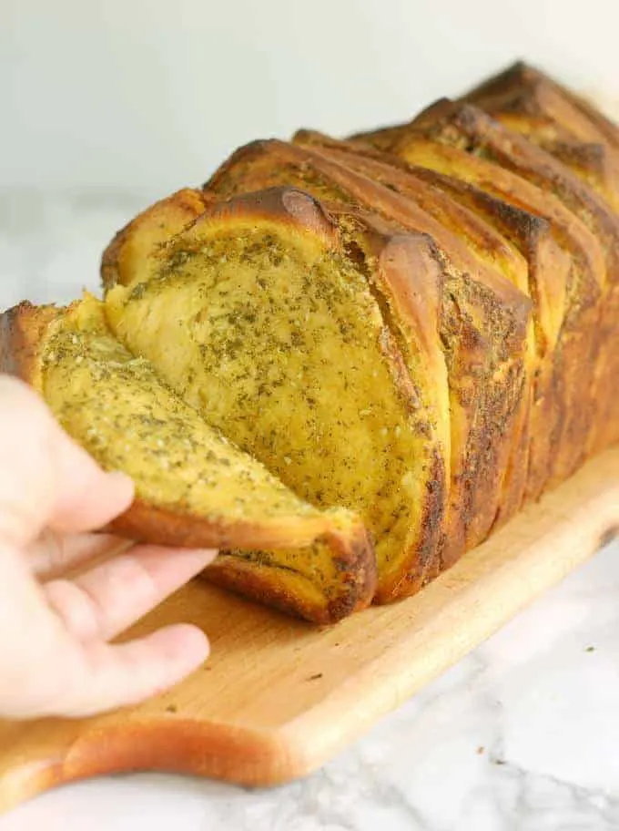 a hand pulling a slice of bread from pumpkin pull apart loaf