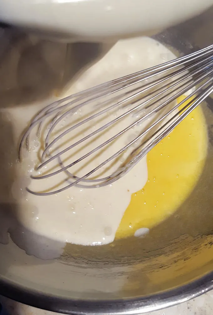 Egg yolks and hot cream in a bowl with a whisk.