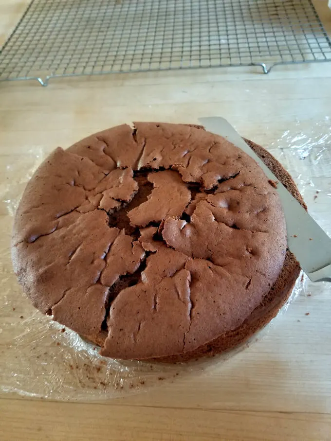a knife slicing the top off of a chocolate cake.