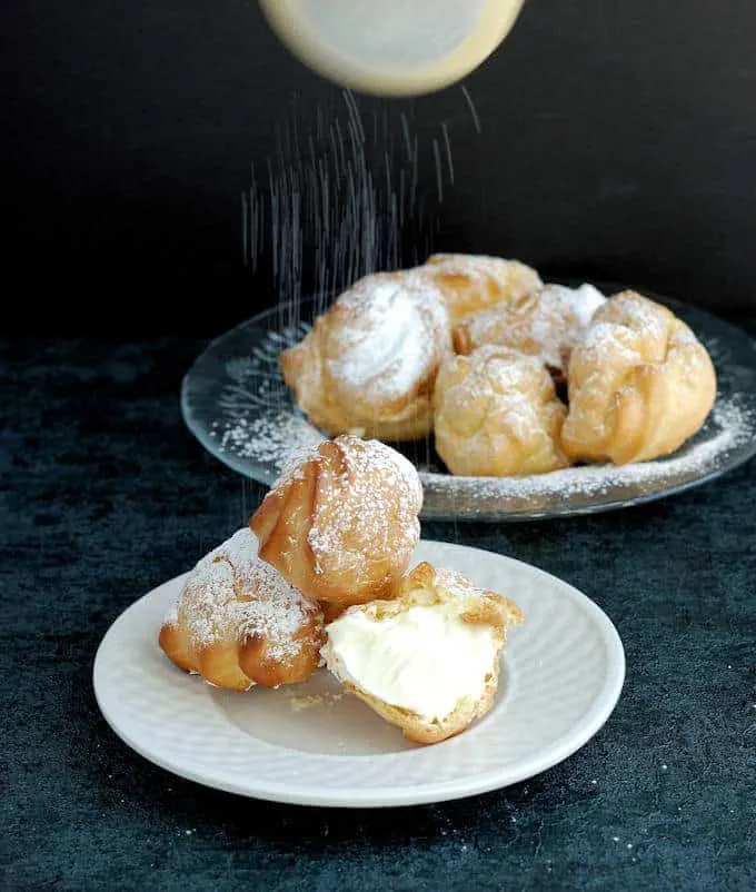 a plate of cream puffs sprinkled with sugar