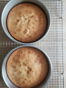 Two white cakes in the pans on a cooling rack.