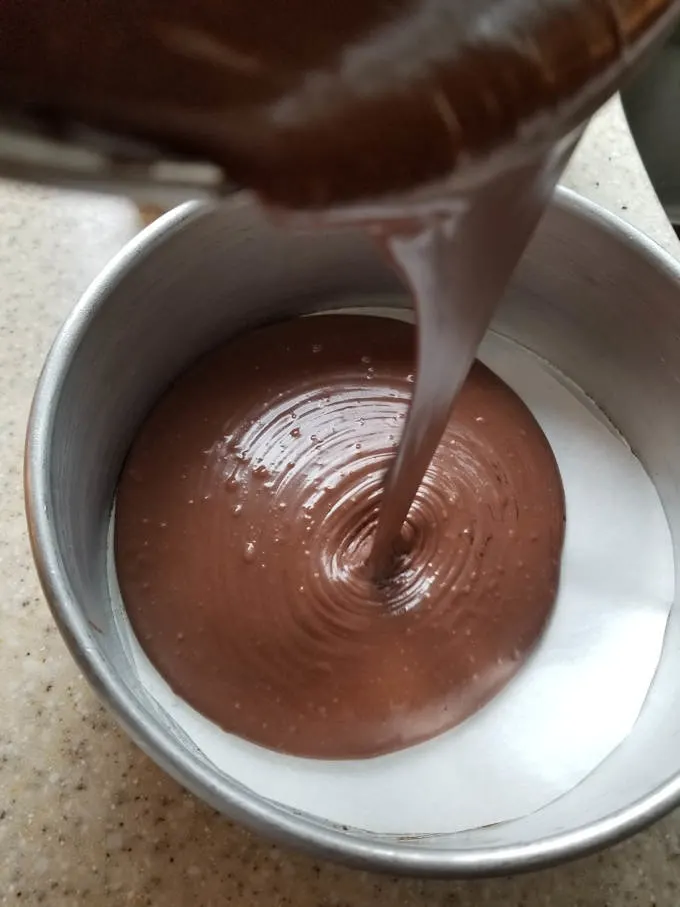 pouring chocolate cake batter into a cake pan.
