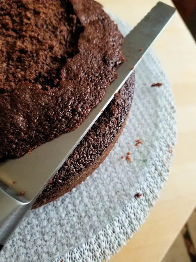 trimming the top off of a chocolate cake layer.