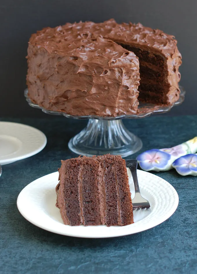 a slice of chocolate cake and a whole cake in the background