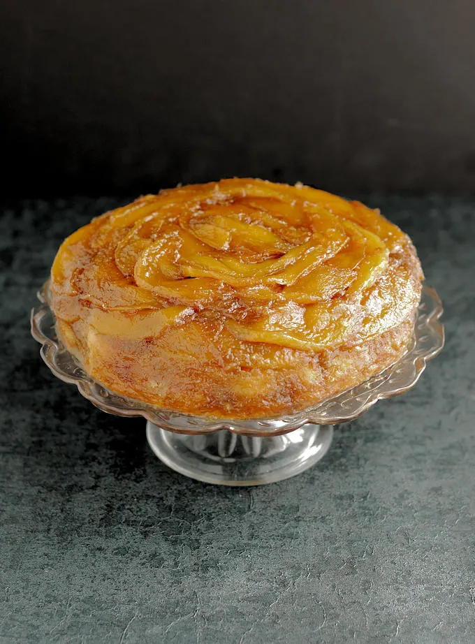 a mango upside down cake on a glass cake plate.