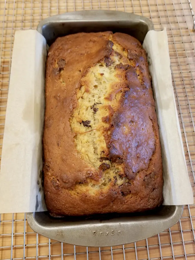 a loaf of chocolate chunk banana bread in a pan on a cooing rack