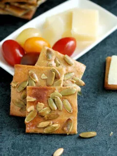 cracker in front of a white plate with tomatoes and cheese.
