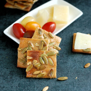 cracker in front of a white plate with tomatoes and cheese.