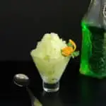 a bowl of green melon granita with an orange twist against a black background