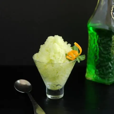 a bowl of green melon granita with an orange twist against a black background