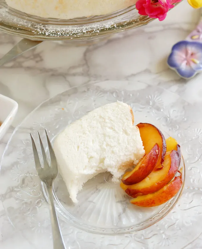 a half eaten slice of angel food cake on a glass plate with a fork and slices peaches