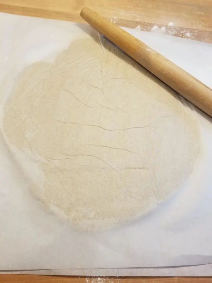 Roll the crust for apple walnut linzer tart between 2 sheets of parchment.