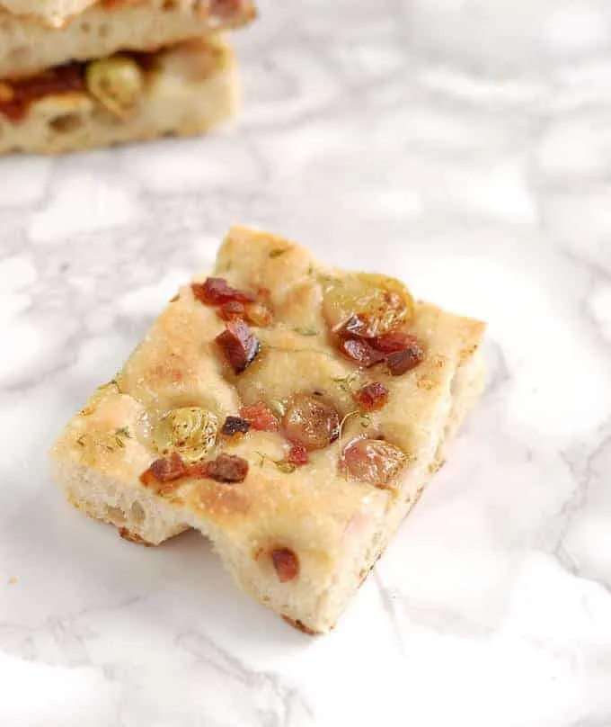 a slice of focaccia with pickled grapes and speck