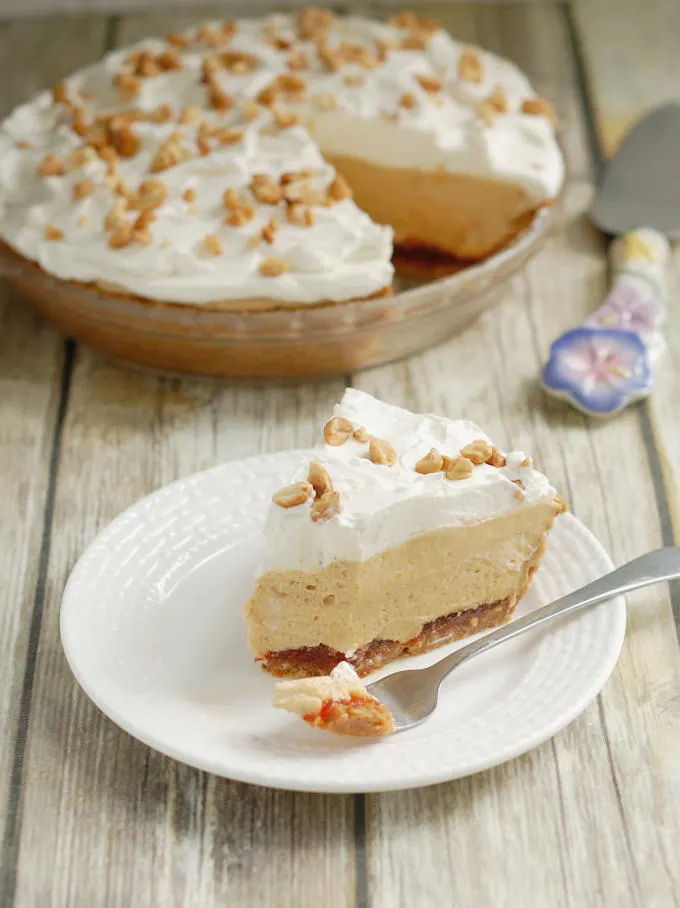 A slice of peanut butter mousse pie with cream and honey roasted peanuts on top