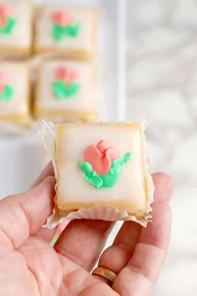 a hand holding a petit four with fondant icing