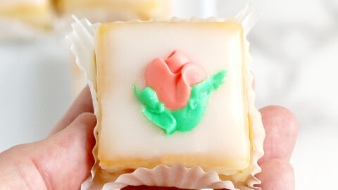 a hand holding a petit four with a pink flower.