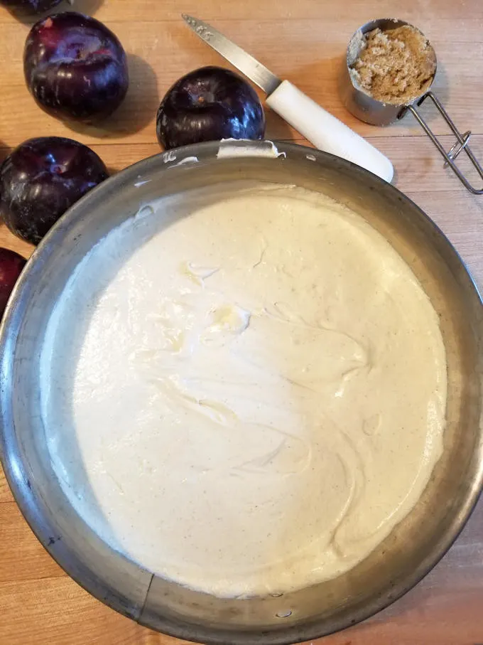cake batter in a pan with plums on the side