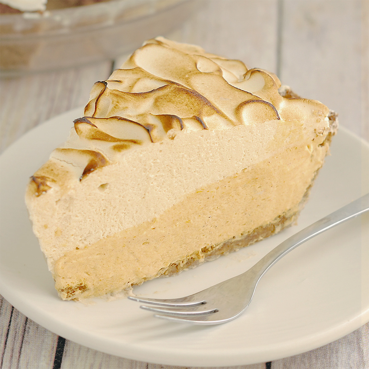 a slice of pumpkin mousse pie with brown sugar italian meringue topping on a white plate.