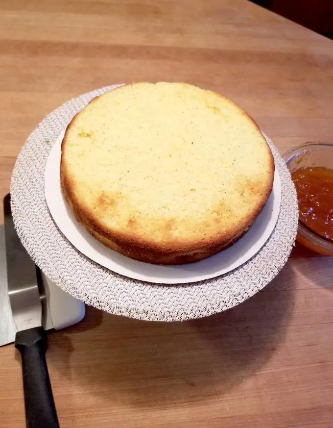 white chocolate sponge cake on a cake turntable with a bowl of apricot preserves.