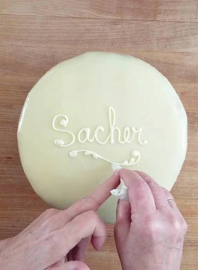 writing the word sacher with white chocolate on a cake.
