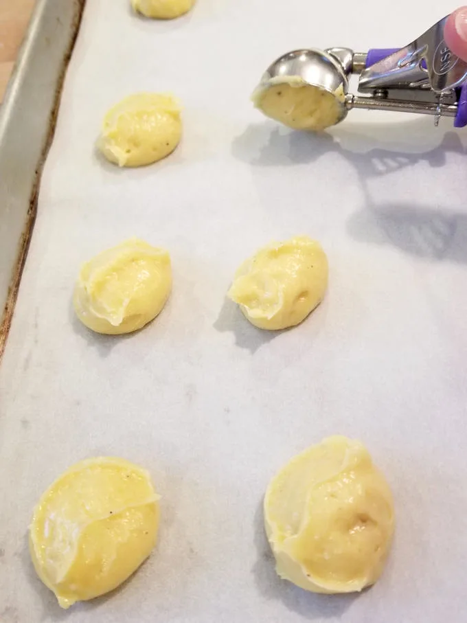 scooping cheesy gougeres into a sheet pan