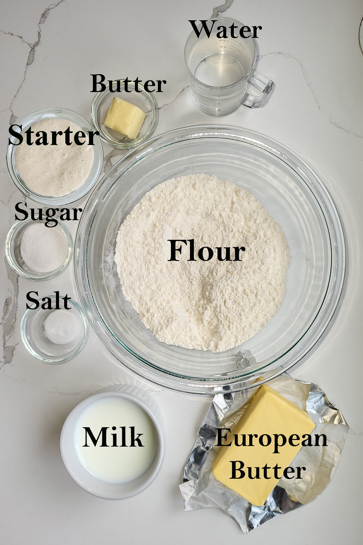 ingredients for sourdough croissants in glass bowls on a white surface.