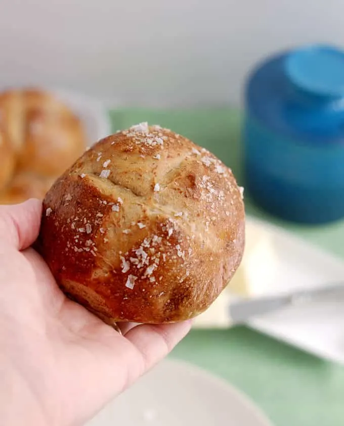 a hand holding a malt and rye pretzel roll