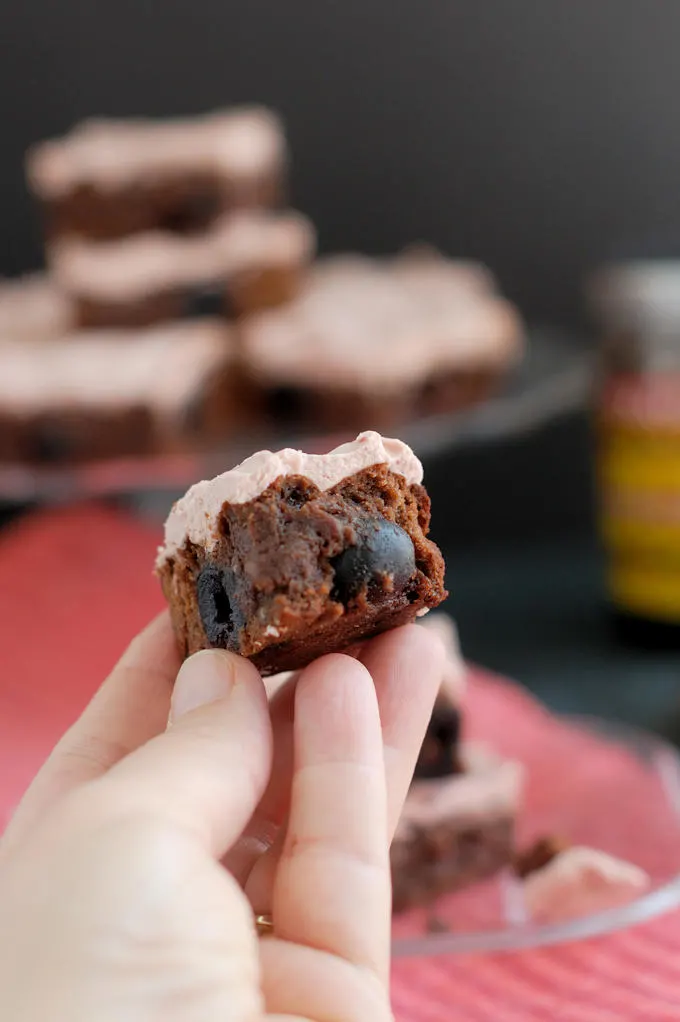 a hand holding a bite of Chocolate Cherry Brownie