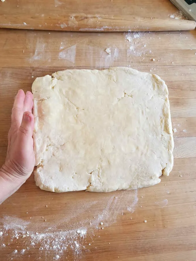 A square of pie dough on a wooden work surface.