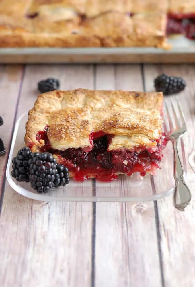 A closeup shot of a piece of blackberry pie with a fork on a glass plate.