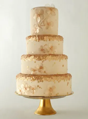 A four tier ivory and gold wedding cake with glitter and flowers