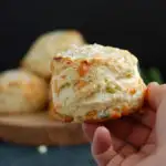 a hand holding a cheese scones against a black background