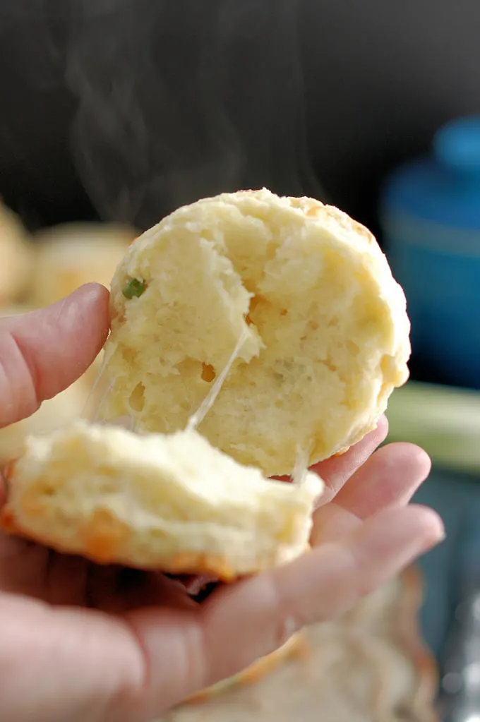 A closeup shot of a split cheese scone. You can see melting cheese and rising steam against the dark background.