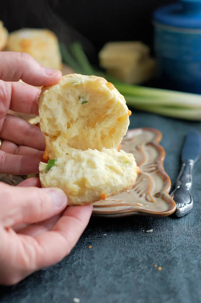 A closeup shot of a warm cheese scone opened up with melting cheese and steam against a dark background.