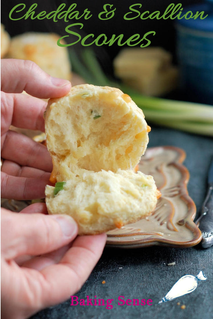 A closeup shot of a warm scone opened up with melting cheese and steam against a dark background. Green text overlay says Irish Cheddar & Scallion Scones