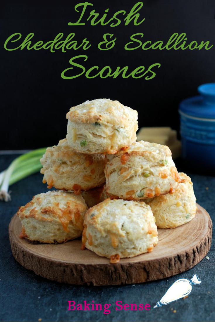 A plate of stacked with scones against a dark background. Green text overlay says Irish Cheddar & Scallion Scones