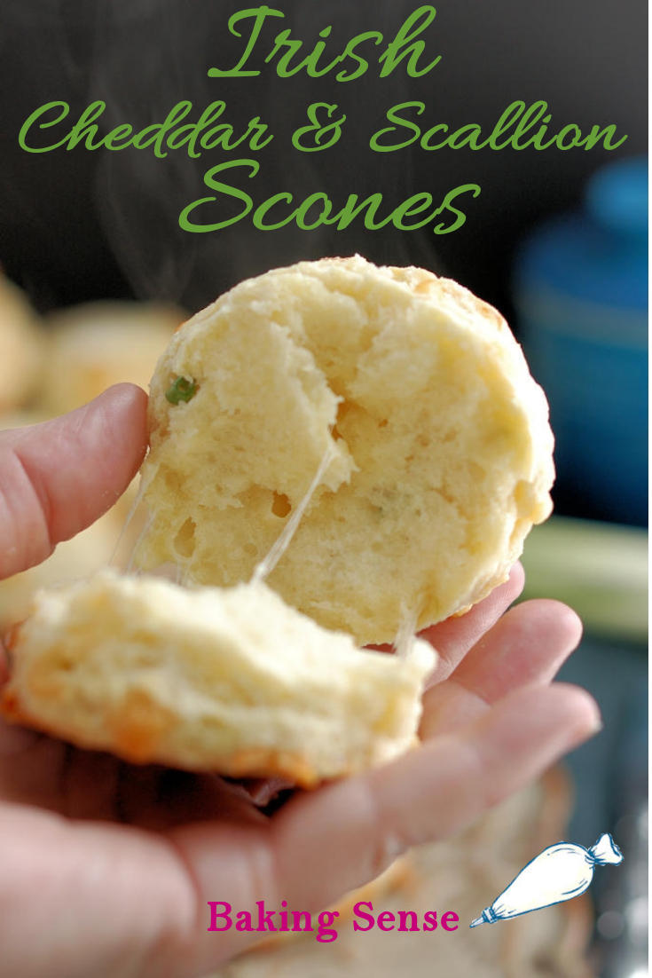 A closeup shot of a warm scone opened up with melting cheese and steam against a dark background. Green text overlay says Irish Cheddar & Scallion Scones