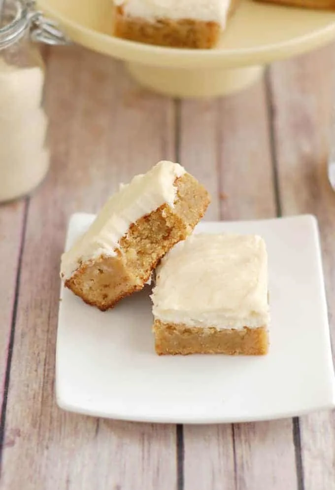two frosted blondies on a white plate.