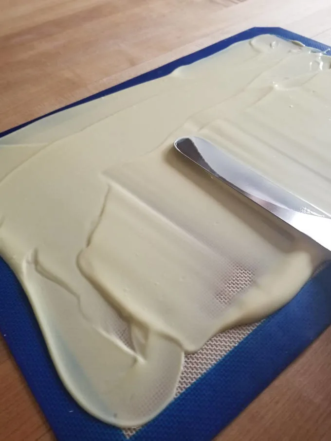 a spatula spreading melted white chocolate on a silicon baking mat
